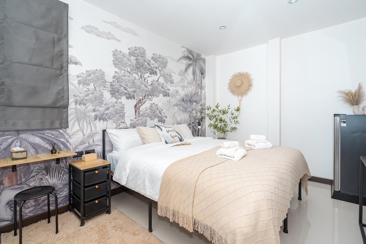 A bedroom with a bed, a desk, a chair, a wardrobe, and a wall with a nature-themed mural.