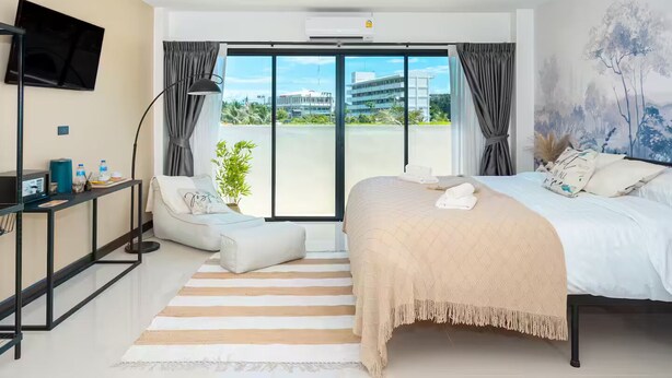 A modern hotel room with a bed, a desk, a TV, and a balcony with a city view.