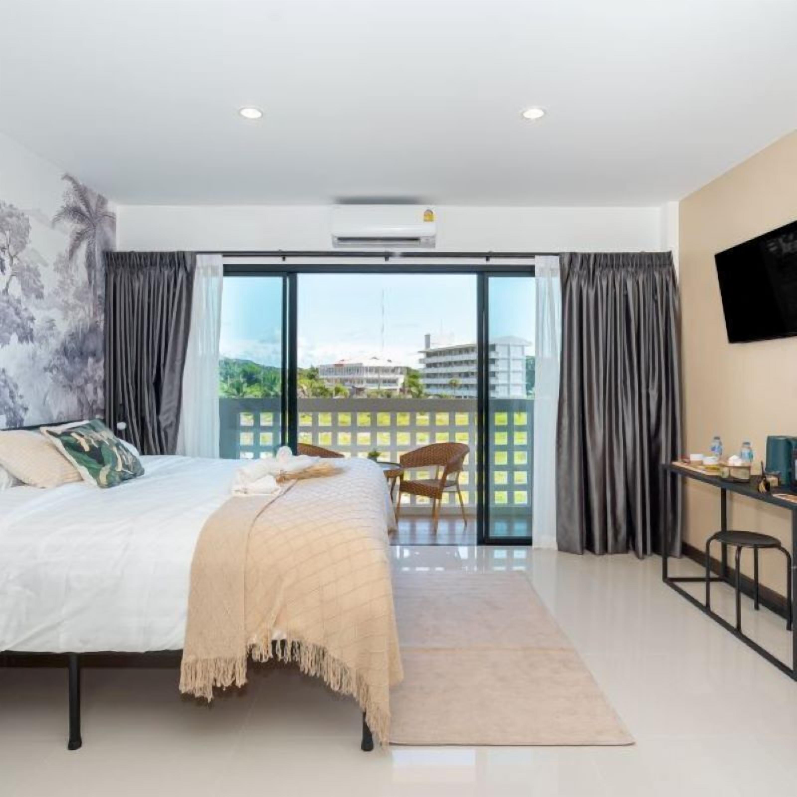 Una habitación de hotel moderna con una cama grande, un escritorio y vistas a un paisaje urbano a través de un ventanal.
