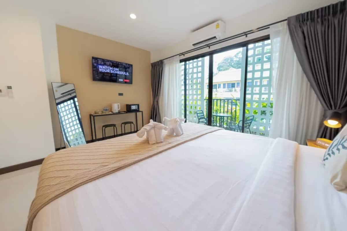A hotel room with a large bed, a flat-screen TV on the wall, a balcony with a view, and a small table with a coffee maker.
