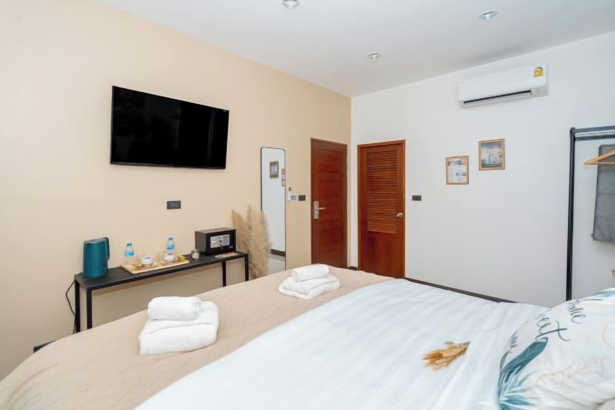 Habitación de hotel con cama, televisor de pantalla plana en la pared, escritorio con computadora y lámpara, y unidad de aire acondicionado en la pared.
