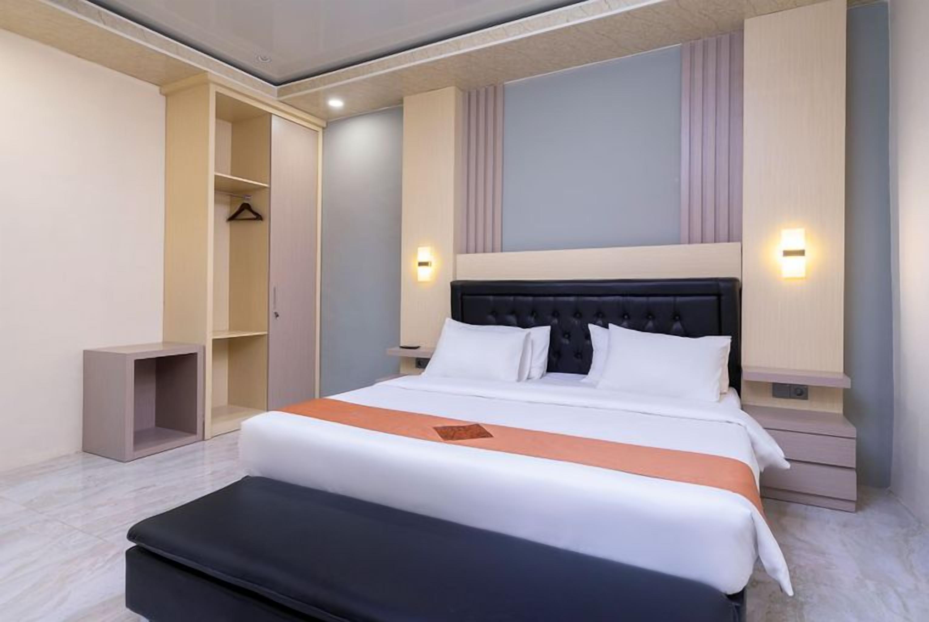 Una camera d'albergo con un letto, comodini, un armadio e una lampada a parete.