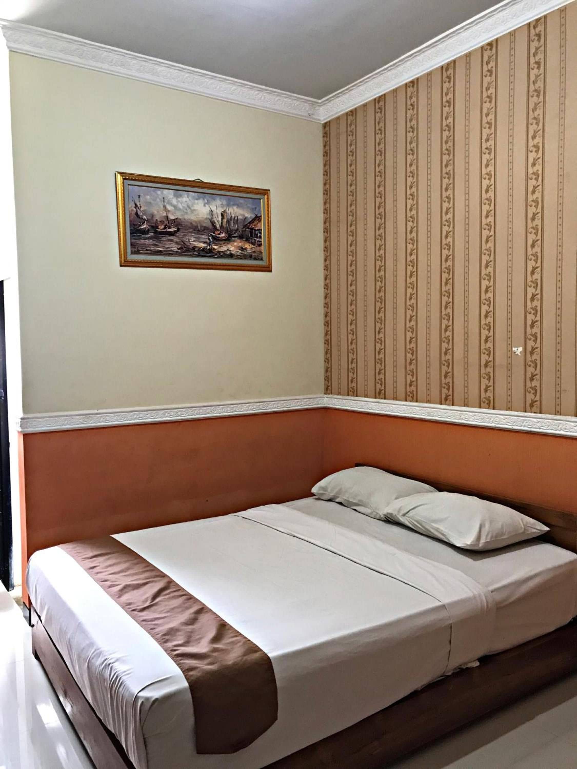 Egy egyszemélyes ágy fejvéggel, felette egy festménnyel, a falakon pedig mintás tapétával.