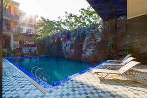 Una piscina con solárium empinado y sillas de descanso, rodeada por un muro de roca con un letrero.