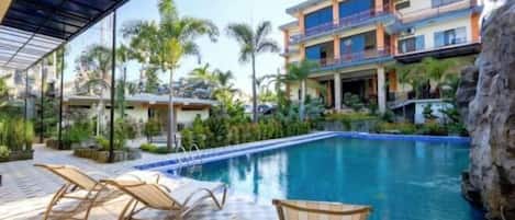A hotel with a swimming pool, lounge chairs, and a covered patio area.