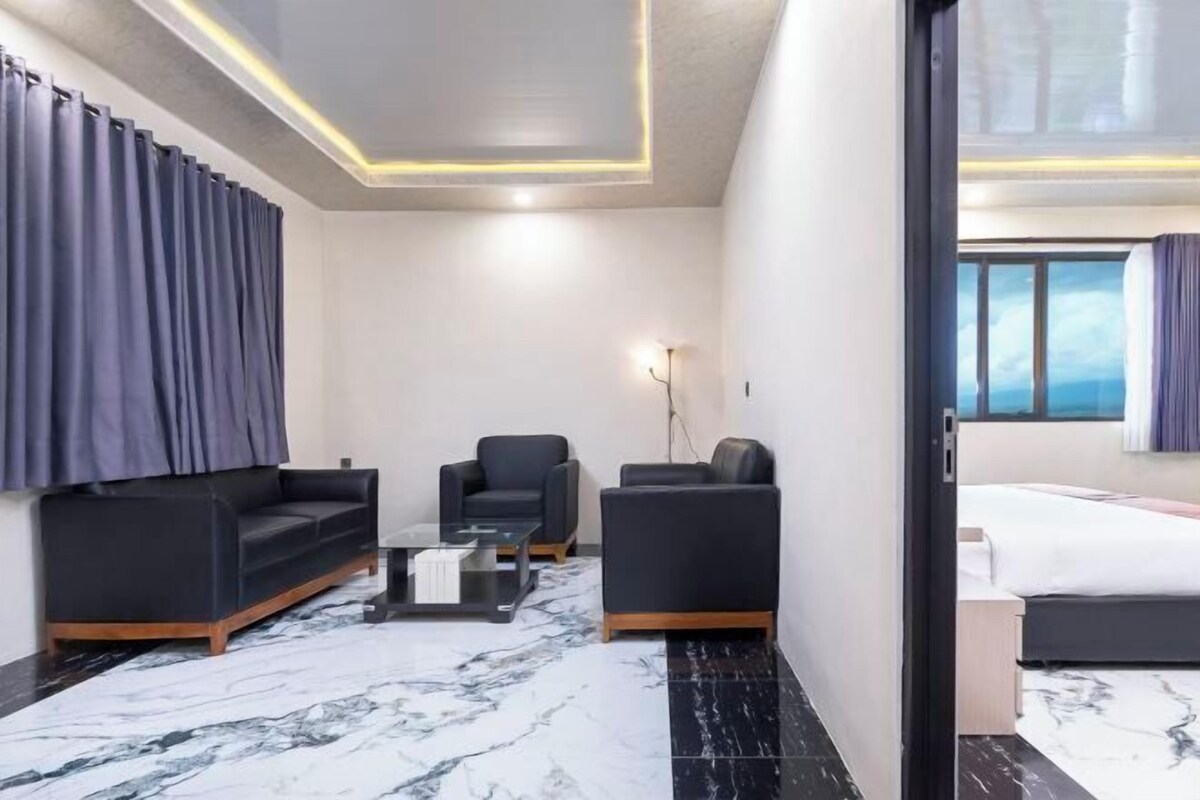 Une chambre d’hôtel moderne avec un sol en marbre, un canapé, un fauteuil, une petite table et un lit.