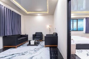 Une chambre d’hôtel moderne avec un sol en marbre, un canapé, un fauteuil, une petite table et un lit.