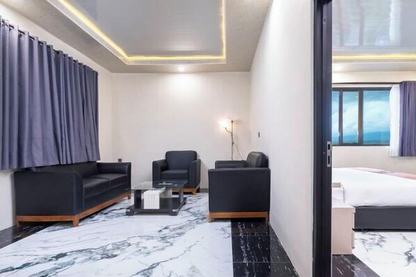 Ein modernes Hotelzimmer mit Marmorboden, einer Couch, einem Sessel, einem kleinen Tisch und einem Bett.
