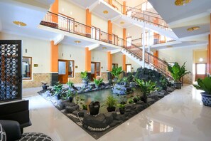 Un atrium à plusieurs niveaux, doté d’un élément décoratif central avec de l’eau, de plantes en pot et d’un escalier.