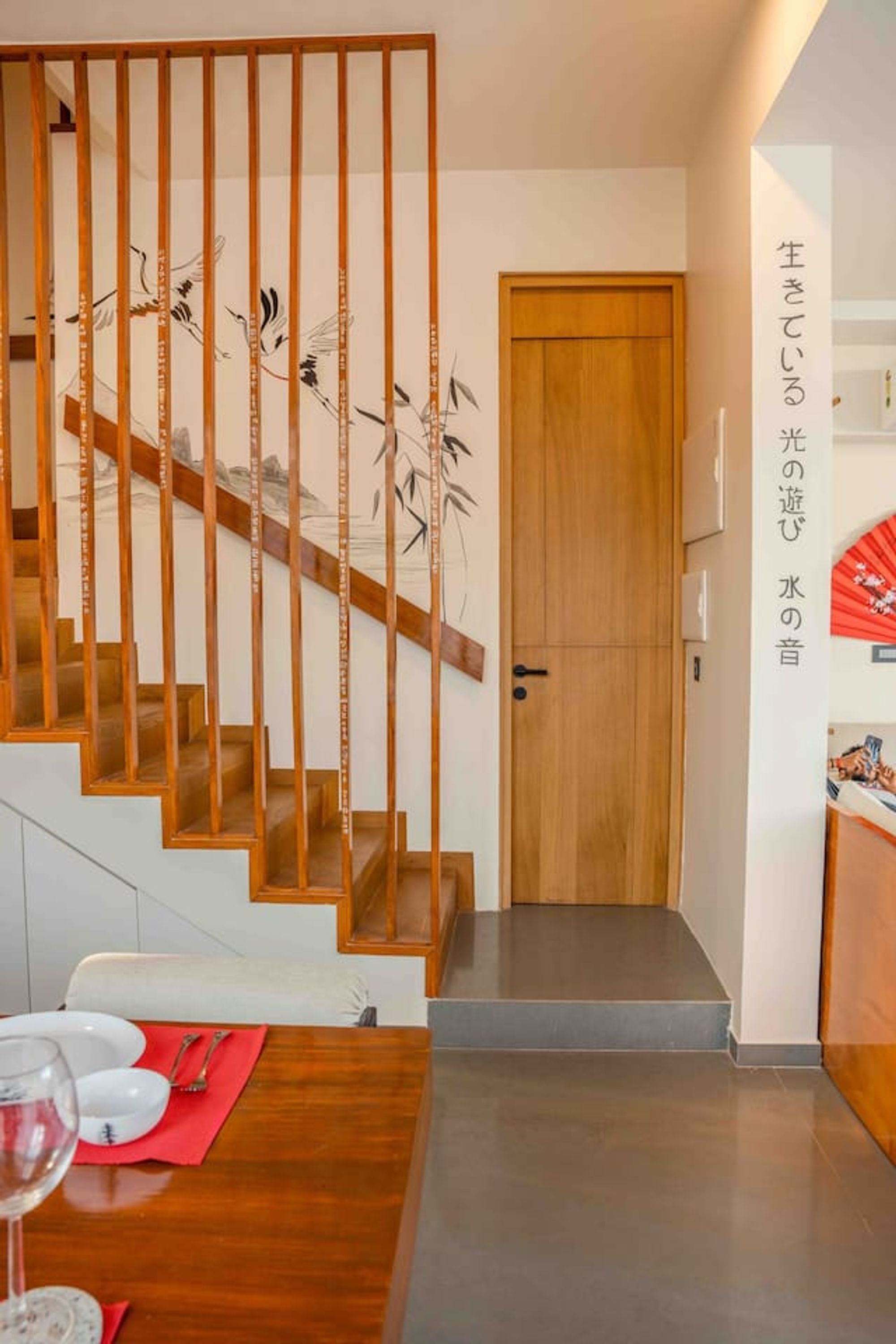 A modern interior with a wooden staircase, a dining area with a red placemat, and a traditional Japanese sliding door.