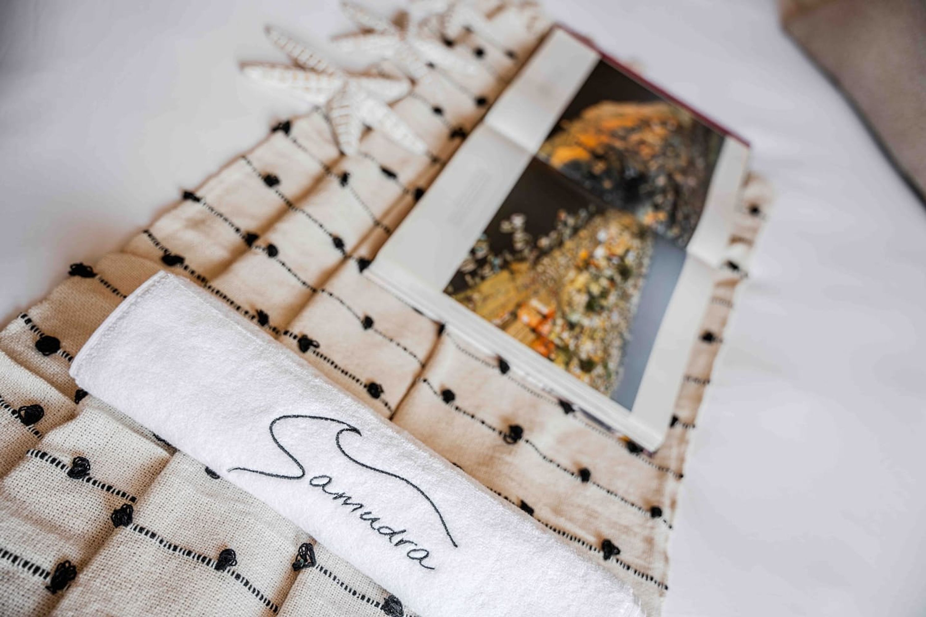 A neatly folded blanket with a name embroidered on it, placed on a bed with a patterned bedspread.