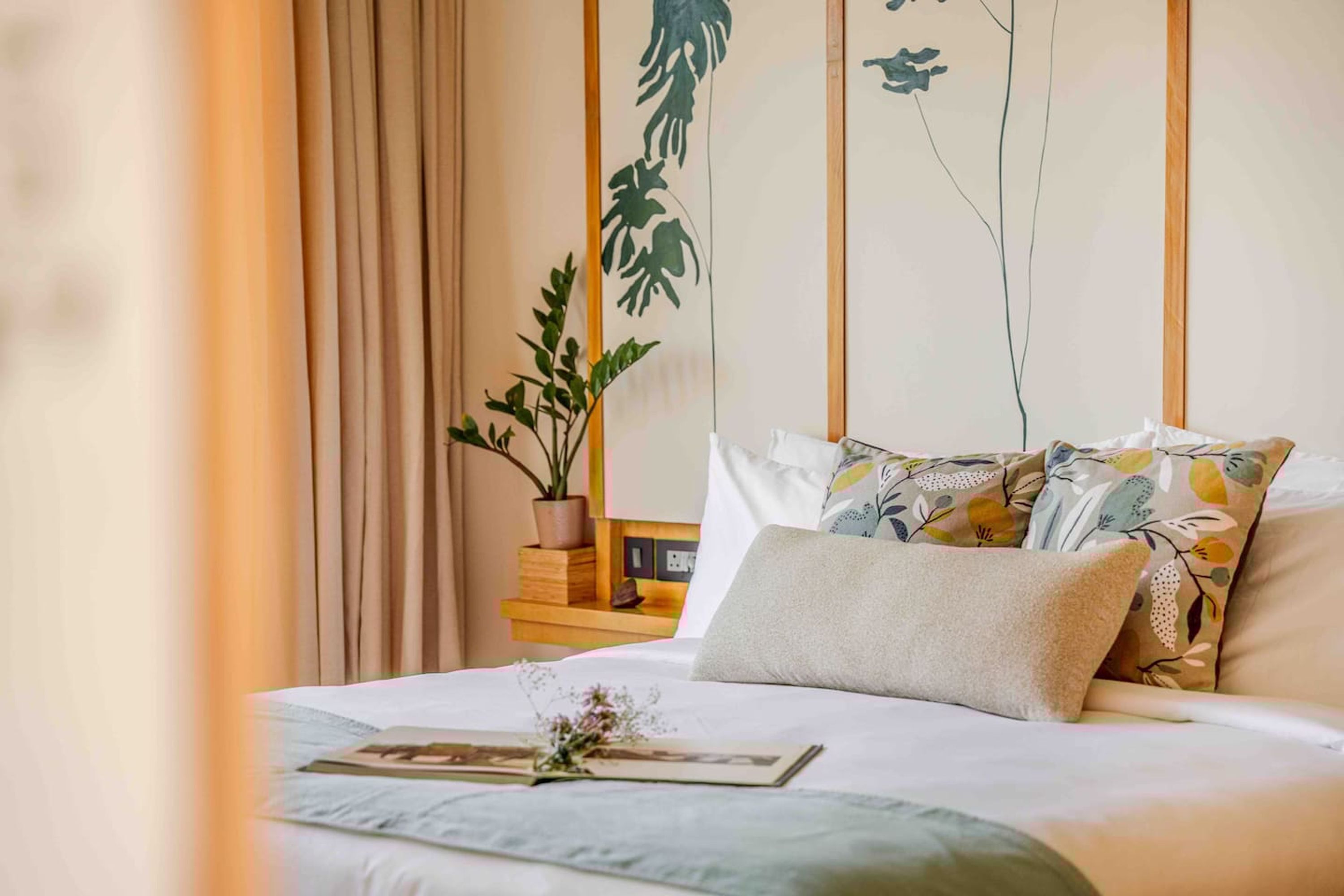 A neatly made bed with a pillow and a small plant beside it.