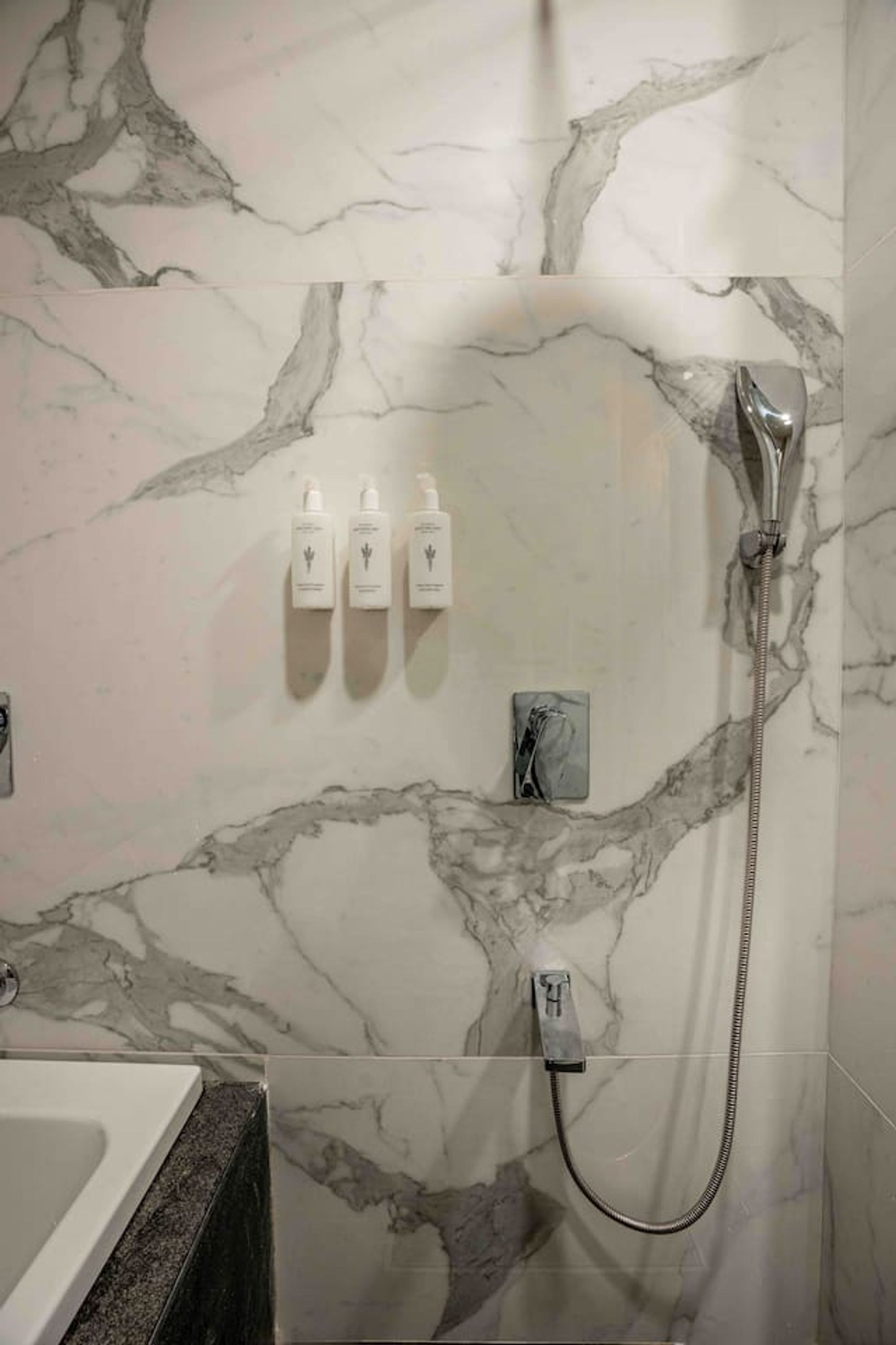 A bathroom with marble walls, a shower, and three toiletries on the wall.