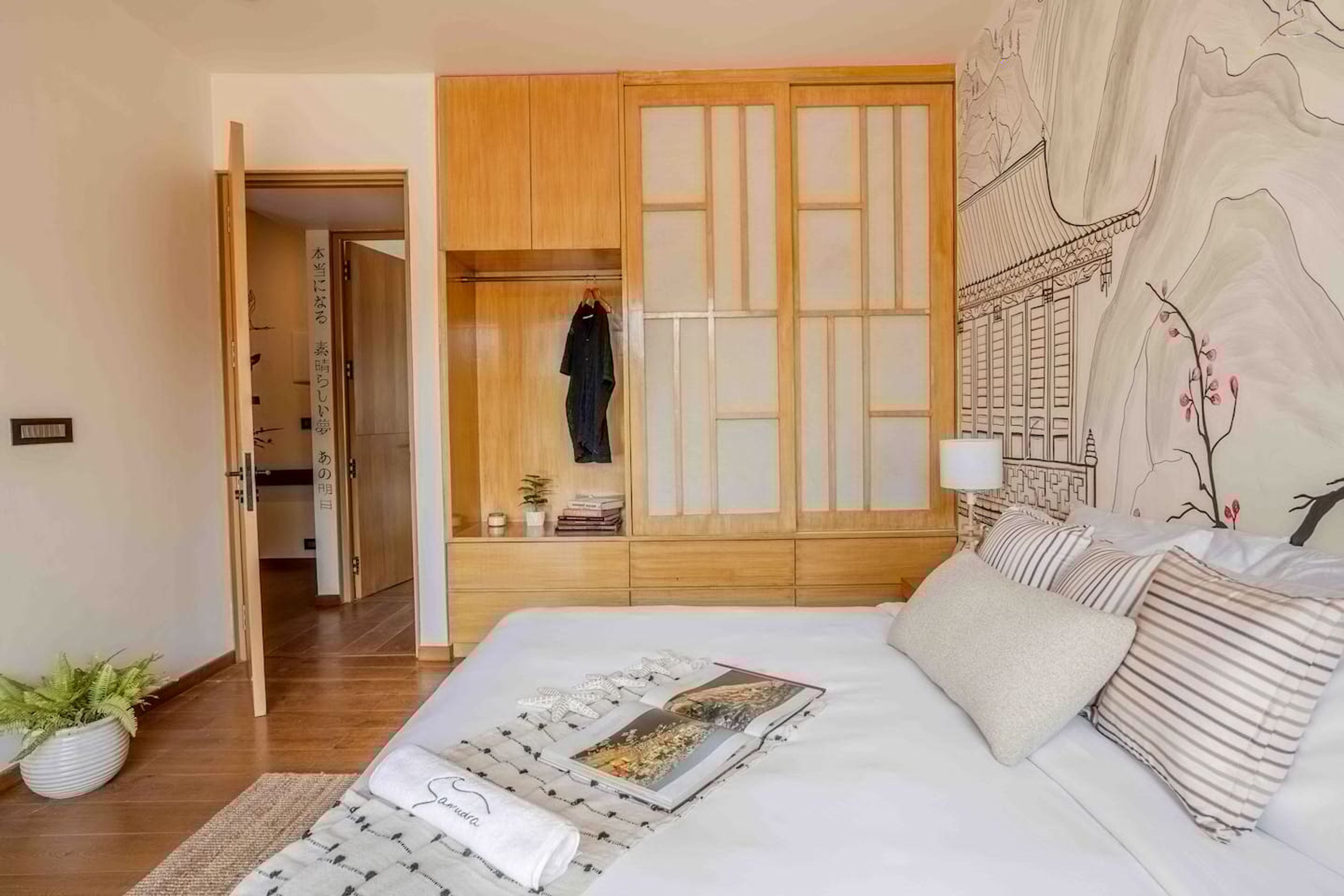 A hotel room with a bed, a wardrobe, a nightstand, and a wall with a mural.