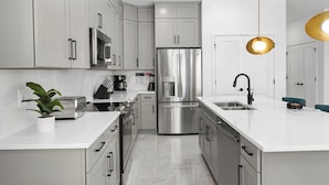 Una cocina moderna con electrodomésticos de acero inoxidable, muebles blancos y una isla central con pileta.