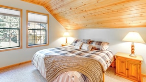 A bedroom with a sloped ceiling, a bed with a checkered bedspread, two bedside lamps, and a wooden nightstand. - Deck w/ Mountain Views: Cabin in Bear Valley! (Bear Valley)