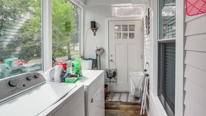 A laundry area with a washing machine, a drying rack, and a window with a view of trees.