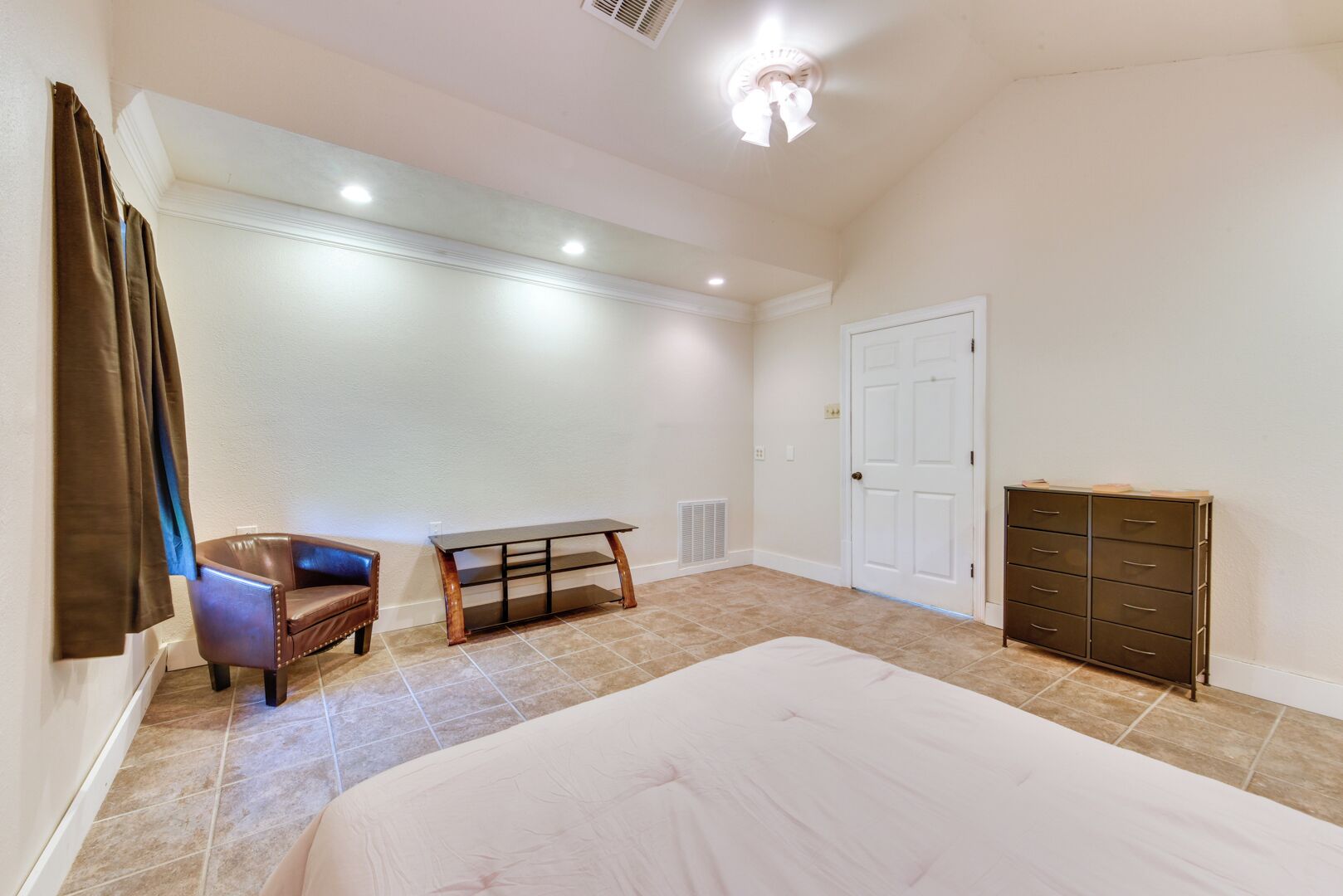 Une chambre à coucher avec un lit, une chaise, une petite table, une commode et une porte.