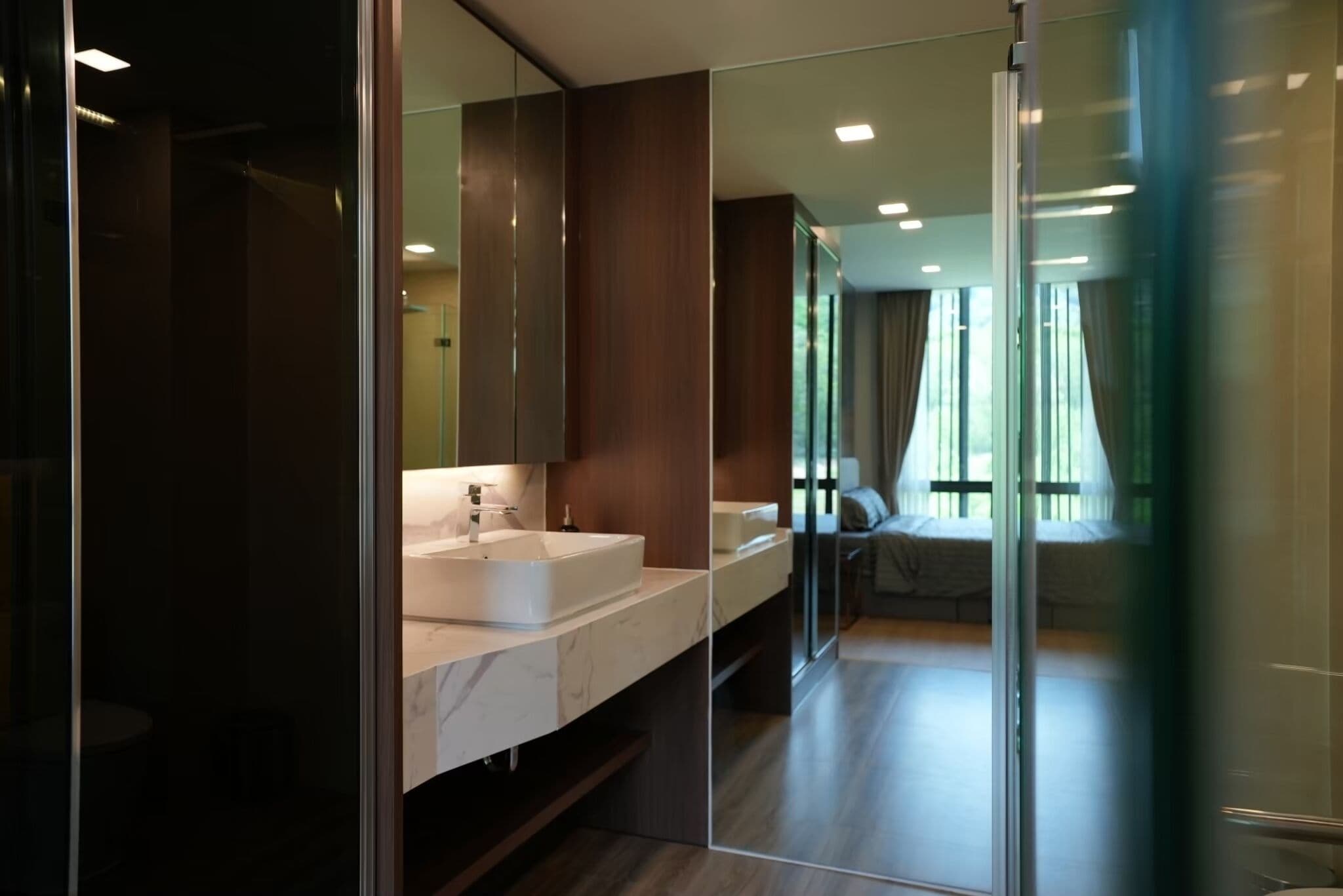 A modern bathroom with a large mirror, a white sink, and a glass partition.