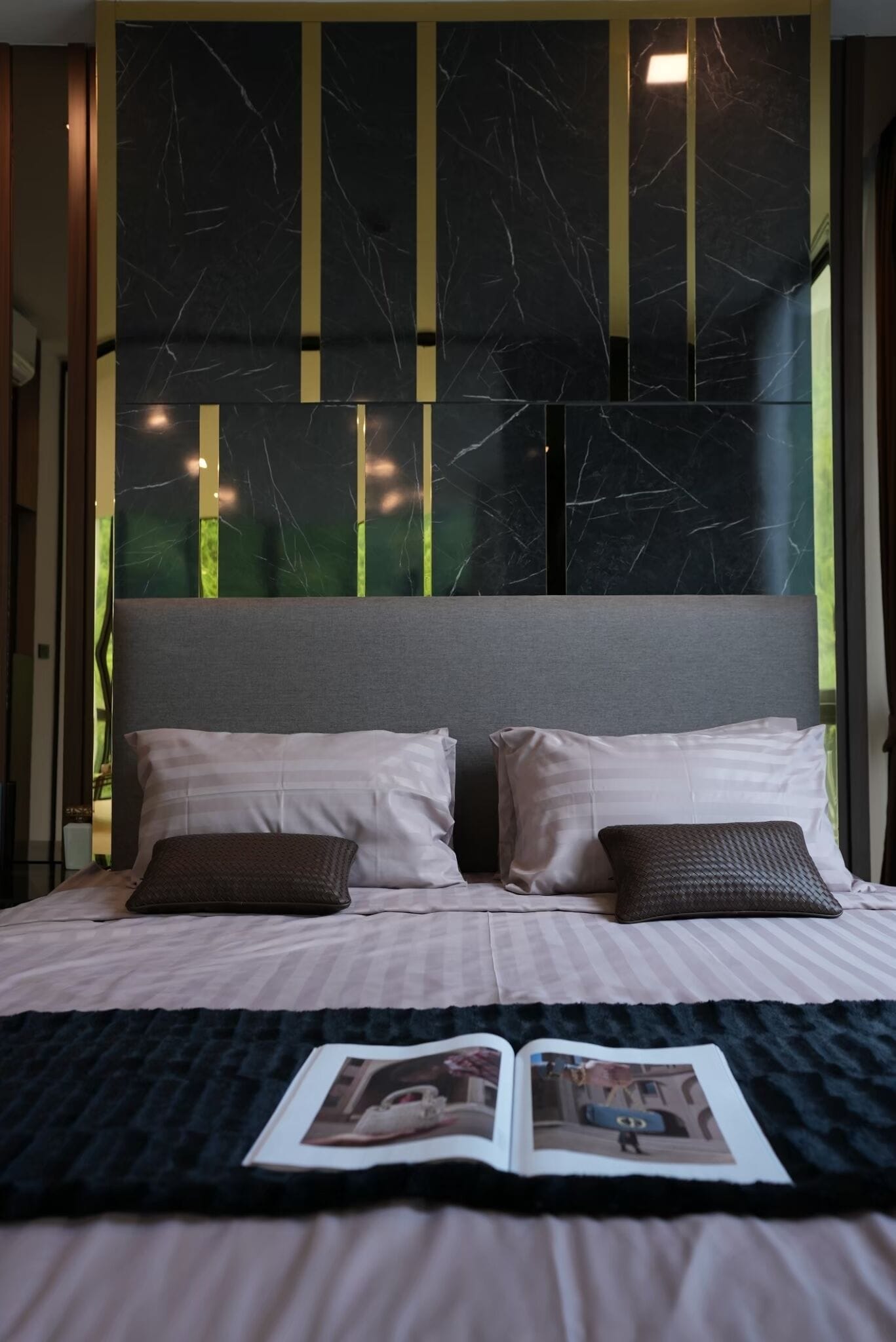 A bed with a grey headboard, two pillows, and a magazine on a dark blanket.