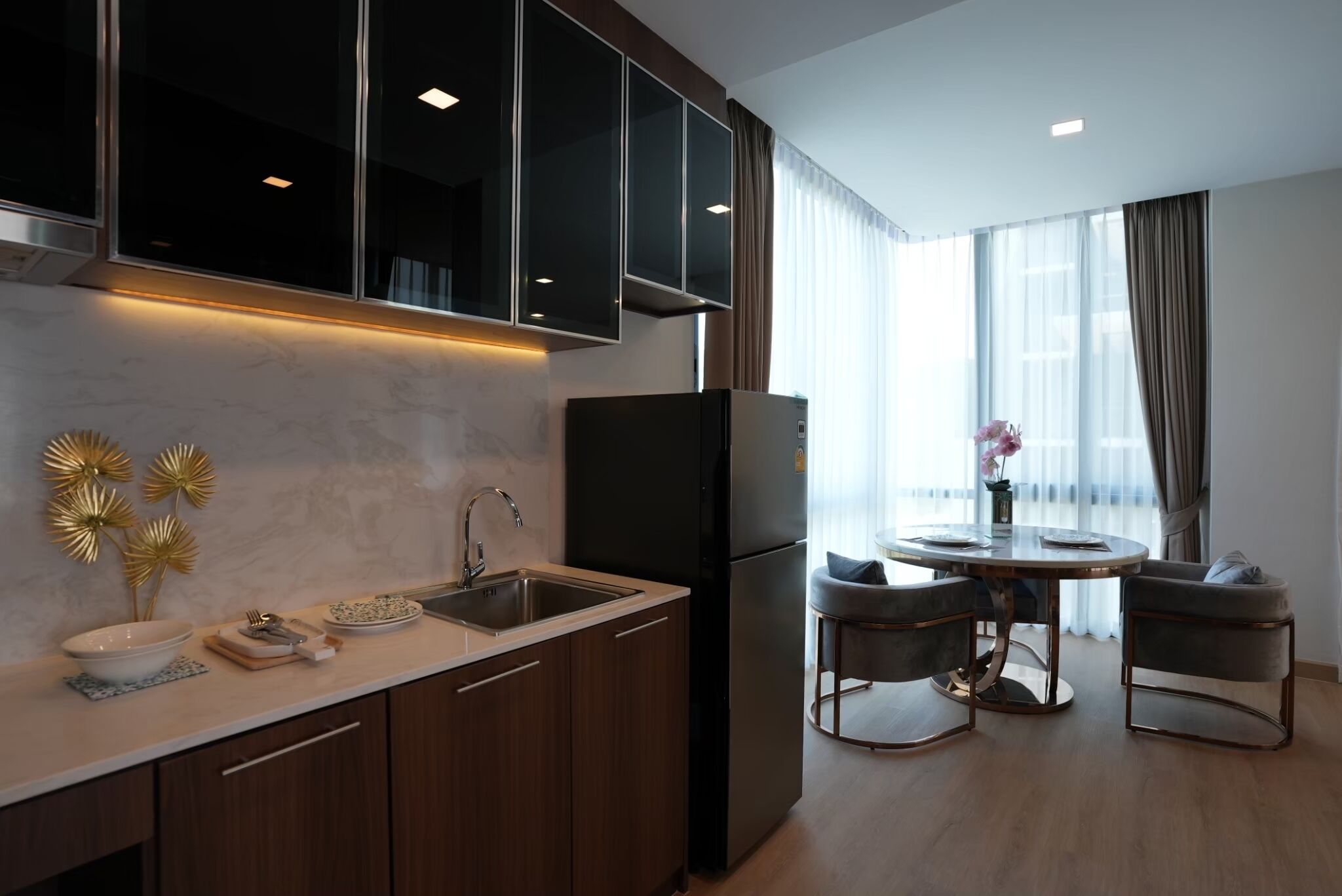 A modern kitchen with dark cabinets, a black refrigerator, and a dining area with two chairs and a table.