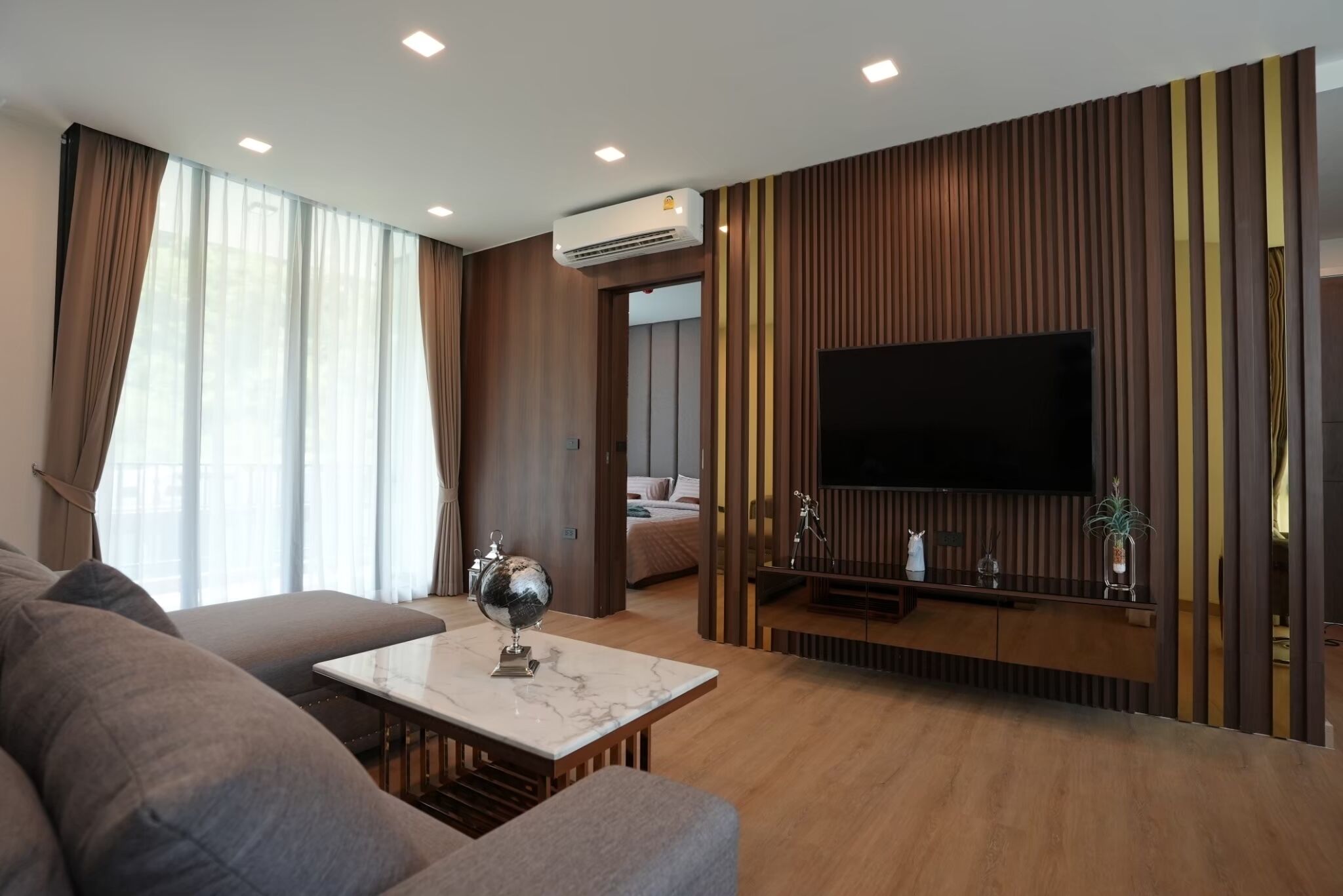A modern living room with a large flat-screen TV, a marble coffee table, and a sofa.