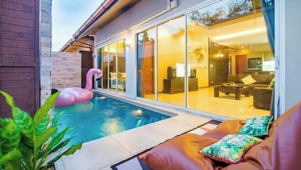 A modern house with a swimming pool, a pink flamingo float, and a glass door leading to a living room with a sofa and a coffee table. - Berich Poolvilla Pattaya (Pattaya)