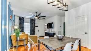 A dining area with a wooden table, clear chairs, a ceiling fan, and a modern light fixture.