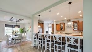 Una cocina moderna con una isla central, taburetes de bar, iluminación colgante y armarios de madera.