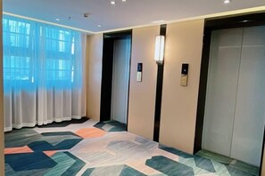 A hotel hallway with an elevator, a patterned carpet, and a window with curtains. - Meitian Holiday Hotel (Shaanxi University of Technology) (Hanzhong)
