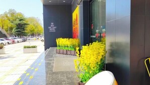 A hotel entrance with a modern design, featuring a dark facade, yellow flower arrangements, and a clear pathway leading to the entrance. - Meitian Holiday Hotel (Shaanxi University of Technology) (Hanzhong)