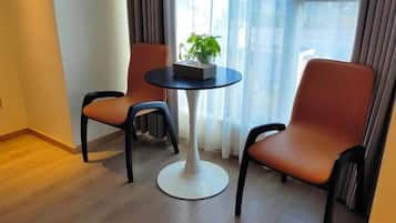 A modern room with two orange chairs and a white table, a potted plant on the table, and a view through large windows.