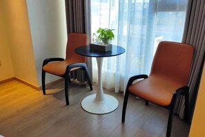 A modern room with two orange chairs and a white table, a potted plant on the table, and a view through large windows. - Meitian Holiday Hotel (Shaanxi University of Technology) (Hanzhong)