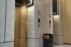 Interior de un ascensor con revestimiento metálico, un panel de control y un cubo de basura.