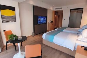 A hotel room with a bed, a TV mounted on the wall, a small table with a chair, and a potted plant. - Meitian Holiday Hotel (Shaanxi University of Technology) (Hanzhong)
