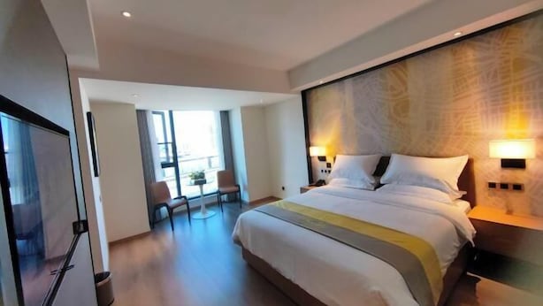 A modern hotel room with a large bed, bedside lamps, a desk, and a view of the city through large windows. - Meitian Holiday Hotel (Shaanxi University of Technology) (Hanzhong)