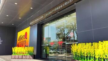 A hotel entrance with a large glass facade, a signboard, and yellow flowers in front.