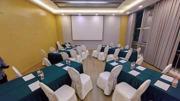 A conference room with multiple tables, white chairs, and a projector screen.