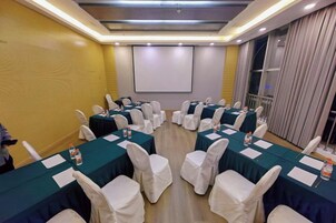Un salón de conferencias con varias mesas, sillas blancas y una pantalla de proyector.