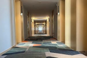 Un pasillo de hotel con alfombra estampada, puertas a ambos lados y techo con iluminación empotrada.