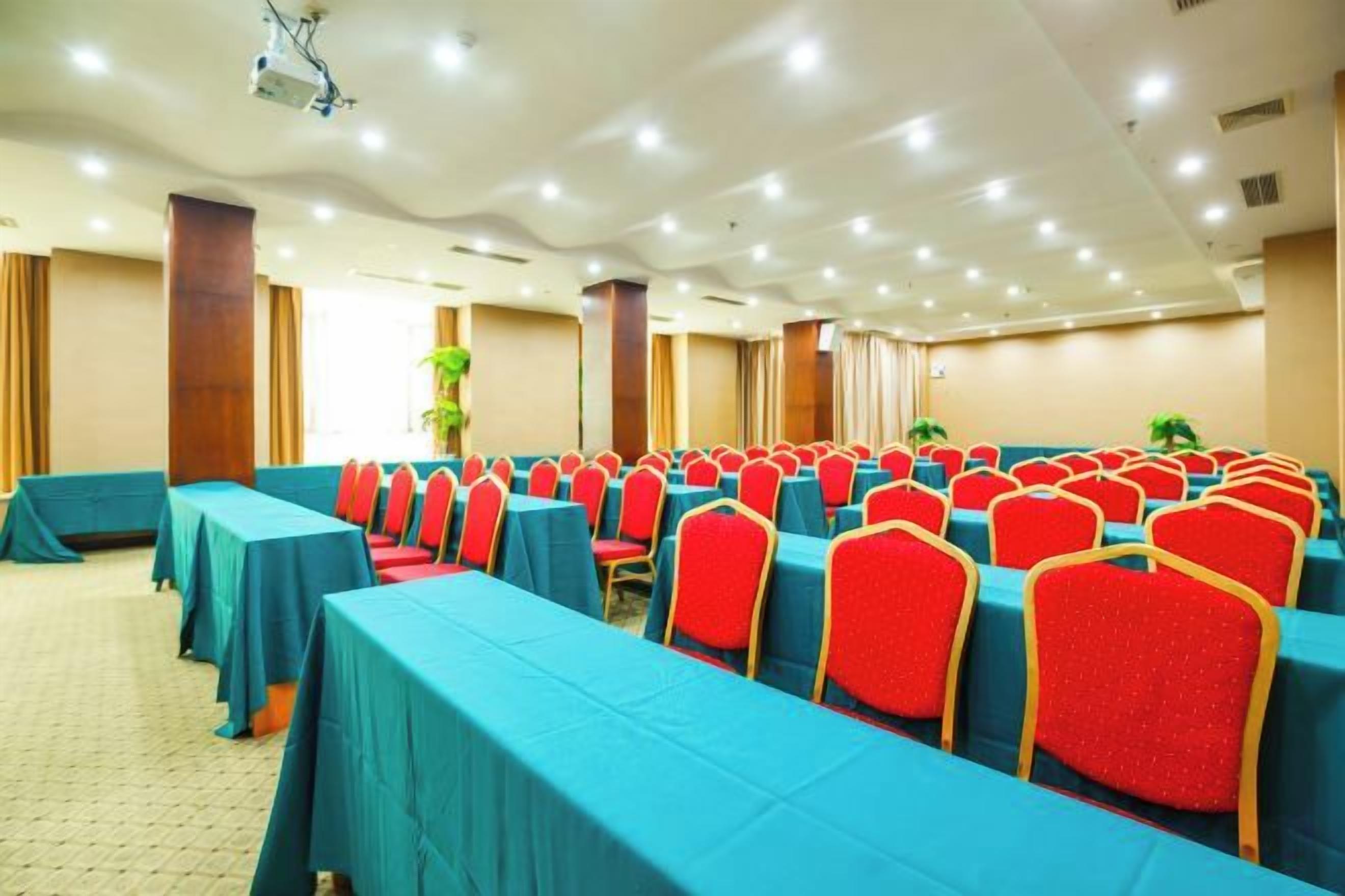 A conference room with rows of tables and chairs, equipped with ceiling lights and a projector.