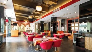 Um restaurante moderno com cadeiras vermelhas e toalhas de mesa xadrez, área de bar e vista da cidade por grandes janelas.