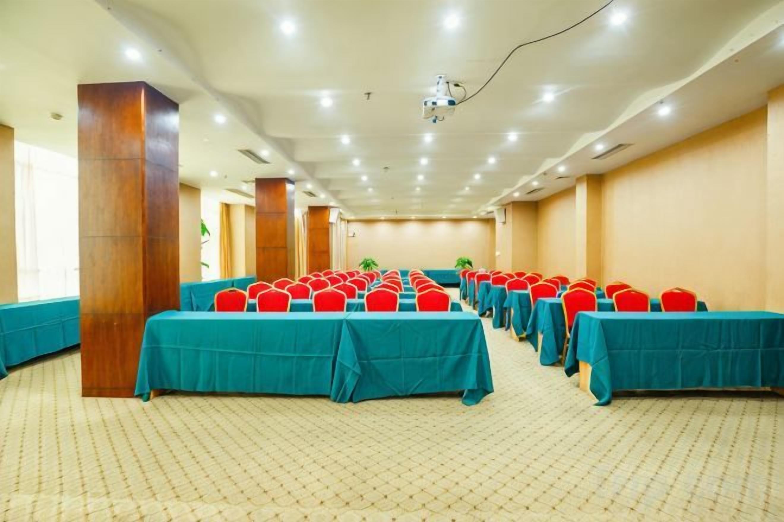 A conference room with rows of tables, chairs, and a projector screen.
