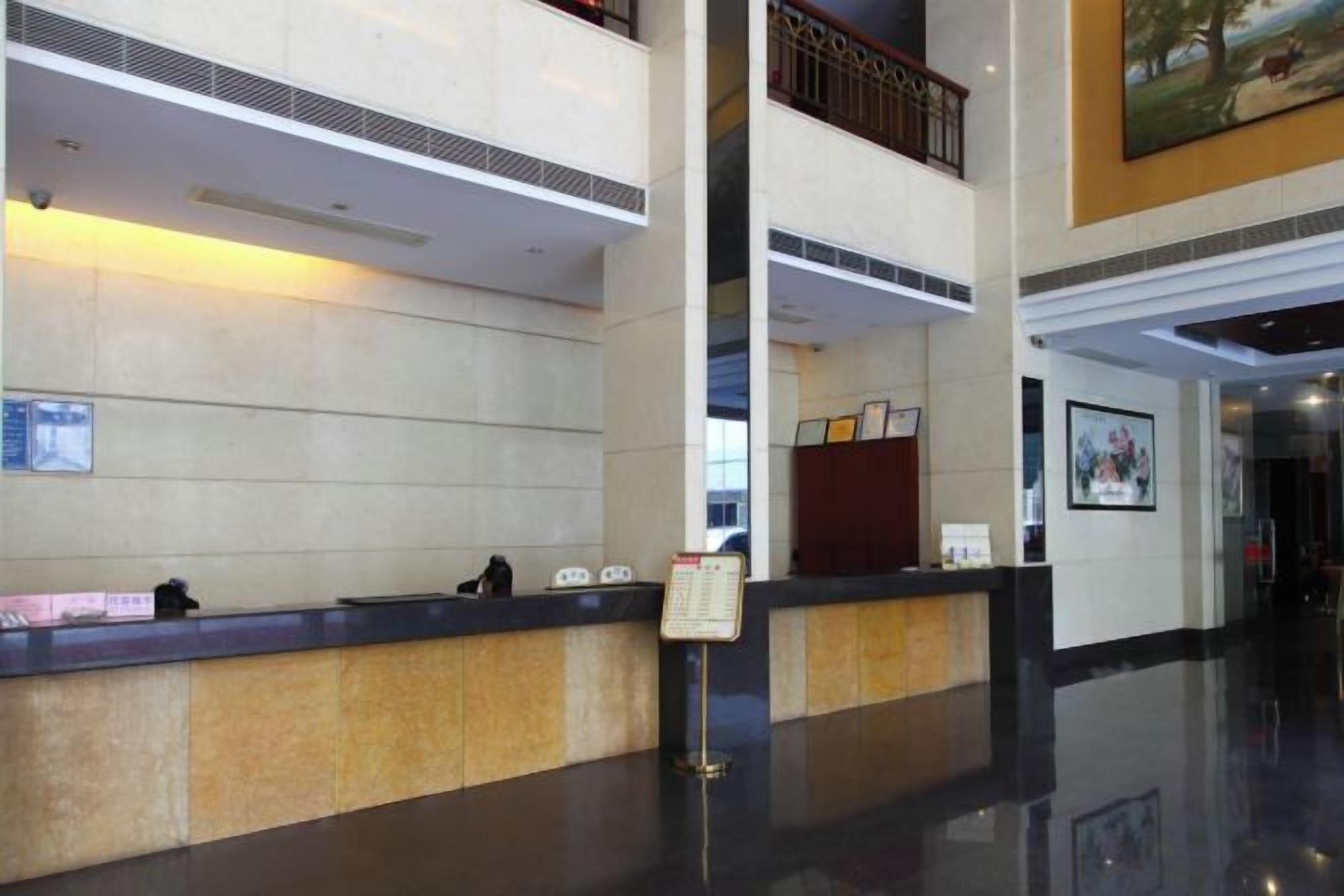 Een hotel receptie met een receptiebalie, een digitaal scherm en een informatiebord aan de muur.