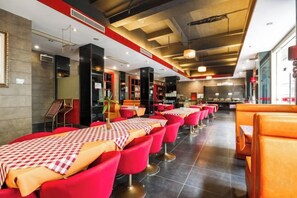 Restaurante com várias mesas e cadeiras, teto alto com vigas aparentes e design de interiores moderno.