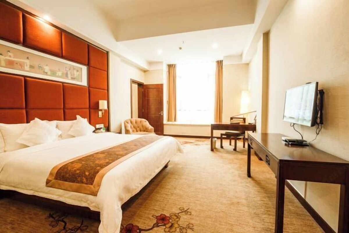 Habitación de hotel con una cama grande, un escritorio, una silla y un televisor.