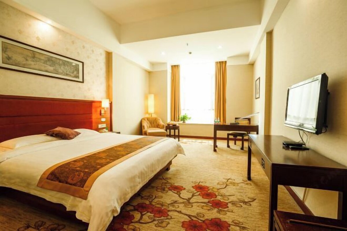A hotel room with a large bed, a desk, a television, and a window with curtains.