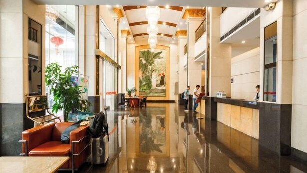 Um hall de hotel com piso lustroso, balcão de recepção, área de estar e uma grande pintura na parede.