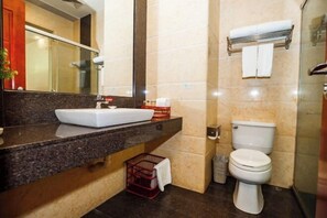 Un baño con encimera de mármol, un lavamanos blanco, un inodoro y una cabina de ducha de vidrio.