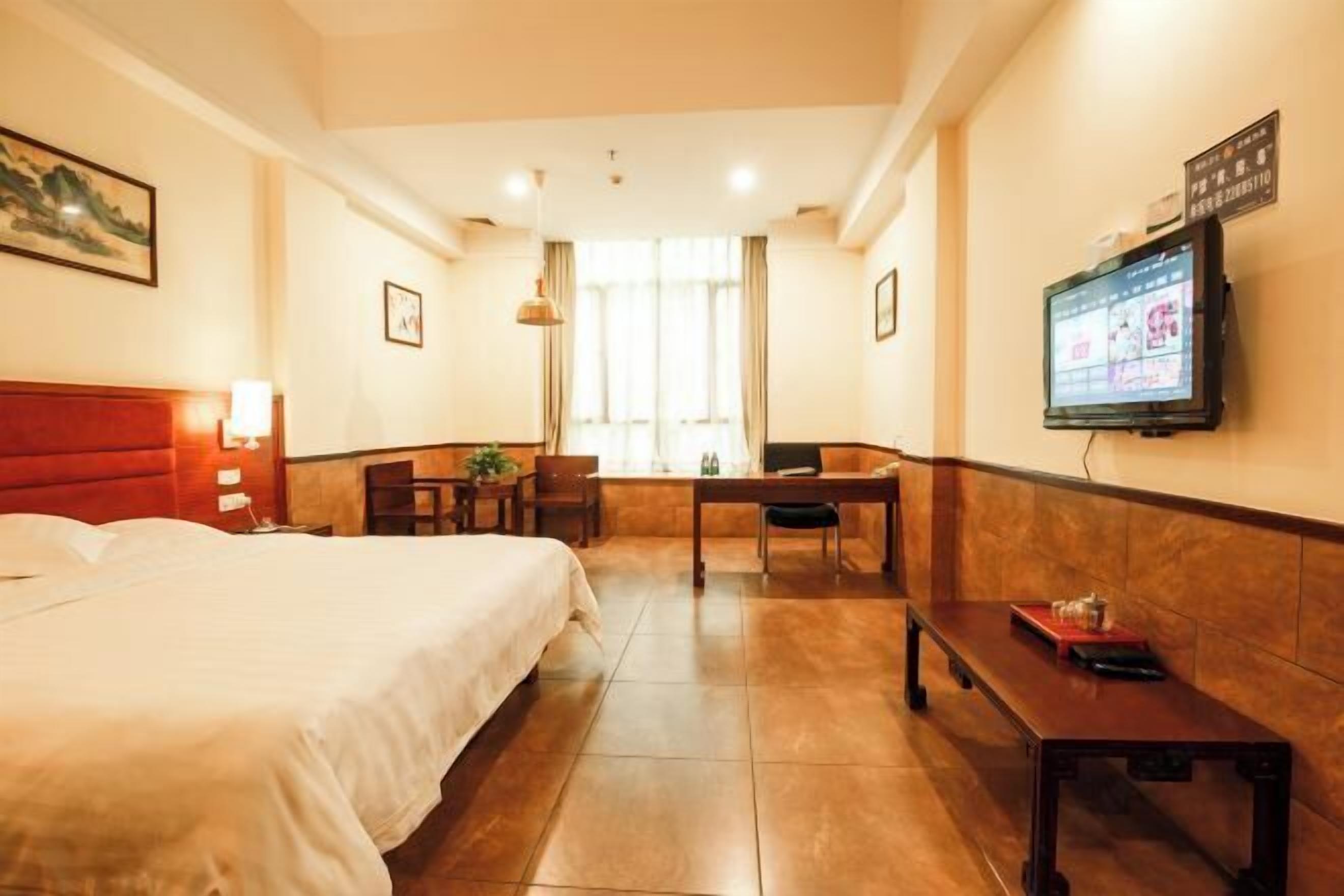 A hotel room with a bed, a desk, a chair, a TV, and a window with curtains.